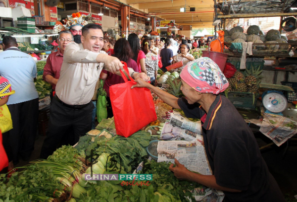 除了派发给购物的市民，陆兆福（左）也派发“福袋”给商贩，献上新年祝福。