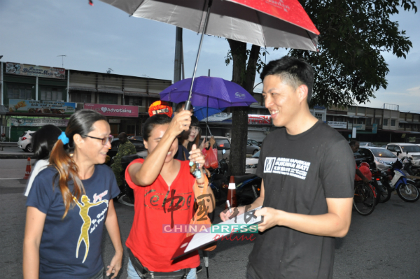 虽然下着雨，韩伟达（右）仍在细雨中向市民讲解反对废除死刑签名运动，希望获得民众签名支持。