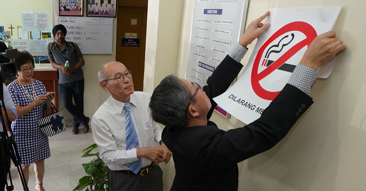 李文材（右起）在郑光辉陪同下，在会所内贴上禁烟海报。