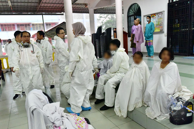 受影响的学生坐在学校附近的清真寺，等待消拯员帮忙冲洗身体消毒。