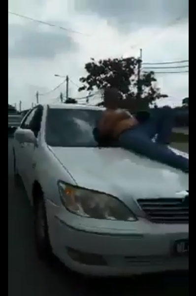 赤裸上身的男子躺卧在轿车前挡风玻璃上“兜风”。（图取自网络视频截图）
