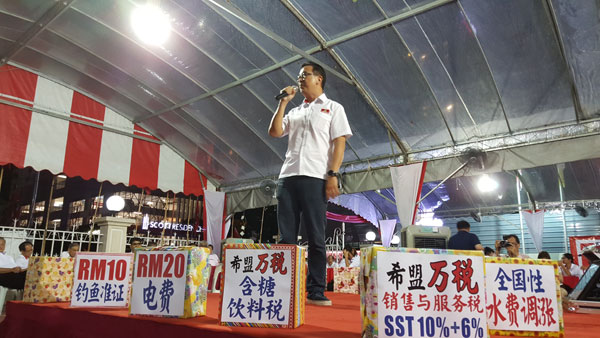 刘华才在中央舞台演说，台上放了讽刺希盟政府政策的饰盒。
