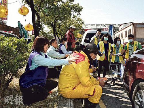 救援人員連日來不眠不休搜索，體力透支，坐在路邊休息，義工見狀上前幫他們按摩放鬆。（圖：明報）
