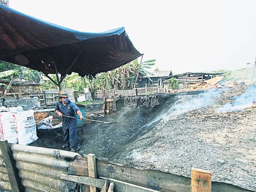 烧炭工友不时翻动木炭窑上的木屑，确保该窑各个角落都是密封。 