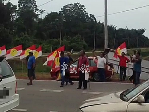 疑是巫統黨員的人士手持黨旗，站在路中阻止車隊經過。