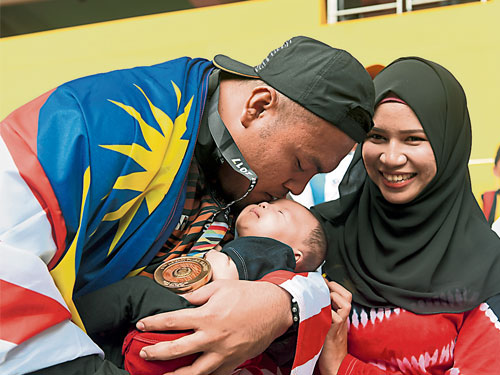  莫哈末茲亞在鉛球賽摘金牌后輕吻孩子的額頭，右為妻子扎菲拉納西爾。