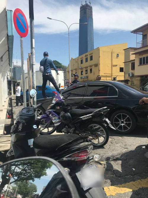  疑非法泊車遭到吉隆坡市政局執法人員鎖輪胎，一一名男子爬到車上以表示抗議。（圖片取自面子書專頁 ）  
