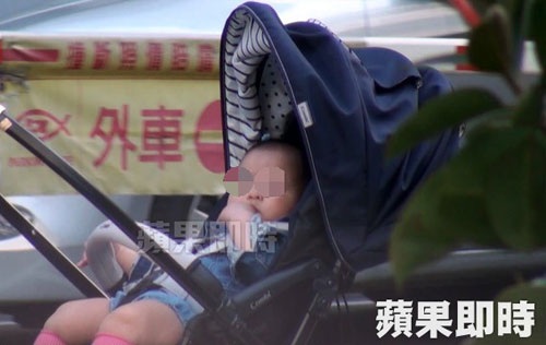哈林女兒坐在嬰兒車裡吮指，大眼圓臉十分可愛。（圖摘自蘋果日報） 