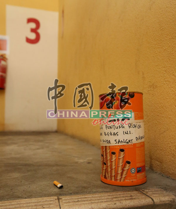 楼梯间发现的烟蒂桶，还贴着要求烟民把烟蒂丢入桶的告示。