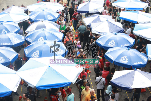 困在长龙中的民众被迫站在大伞外，有者于清晨6时许便开始排队。