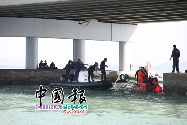 搜救人员将配备带到大桥下，准备吊起车子。