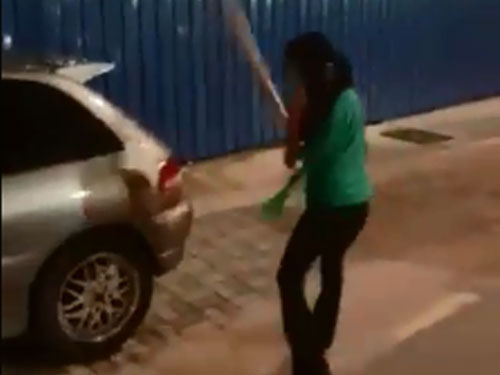 视频中的妇女很凶悍，拿着木棍不知何故，敲打停在路旁的车辆。