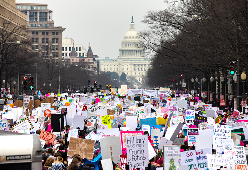 大批妇女周六在宾夕法尼亚大道上参与游行，当中有人举牌指“特朗普是俄罗斯的傀儡”。（欧新社）