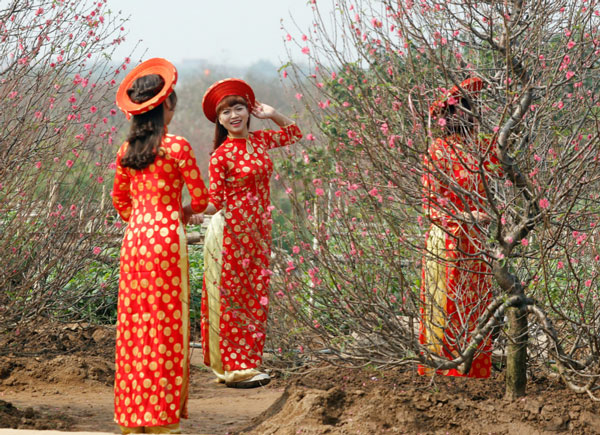 穿着大红传统“奥黛”在花丛拍照的越南女性。