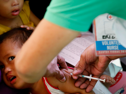 菲律宾红十字会和卫生部官员到马尼拉社区，为幼童接种麻疹疫苗。（美联社）