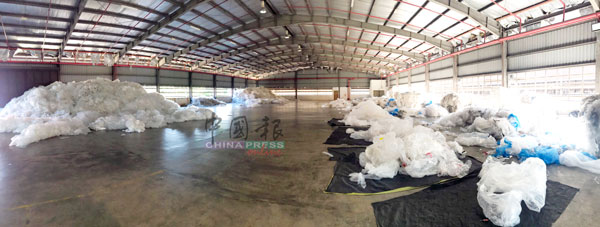 塑料回收厂的厂房宽大，内部的塑料堆积如山。