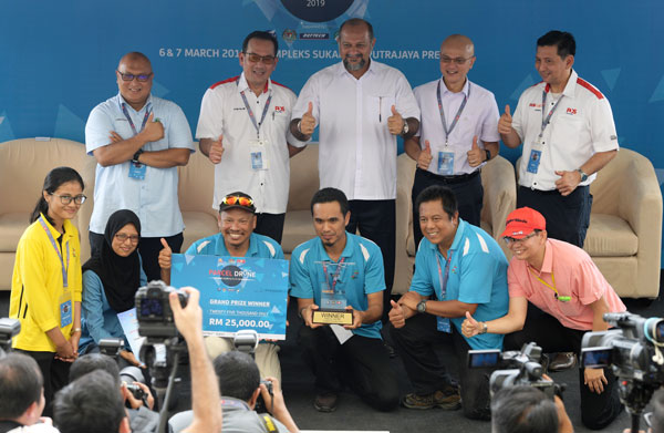 哥宾星（站者左3）颁发奖杯和2万5000令吉的奖金给“无人机送包裹比赛”的冠军队伍。