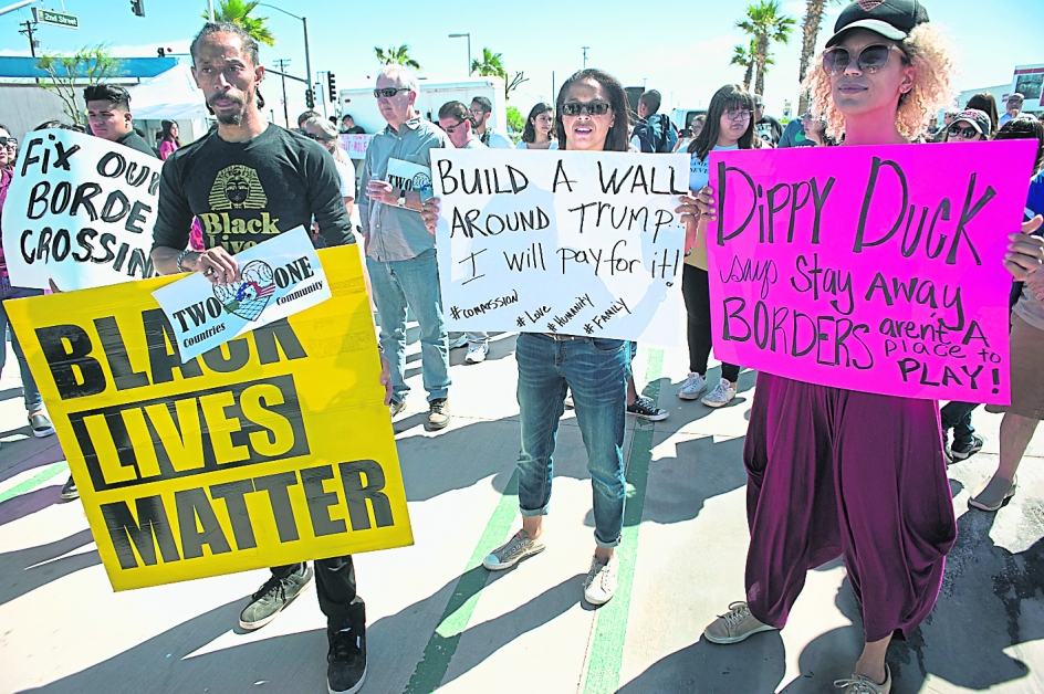 示威者周五在美墨边境的卡莱克西科市高举标语牌，抗议特朗普执意要建美墨边界围墙。（欧新社）