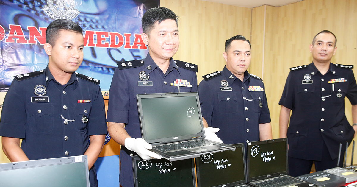 鲁迪（左2）与建功警察向媒体展示，警方取缔马机店后起获的手提电脑。