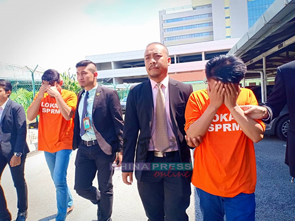 2名身穿橙色衣的嫌犯被反贪会官员带上法庭时，皆以双手遮住脸部以阻挡摄影镜头。
