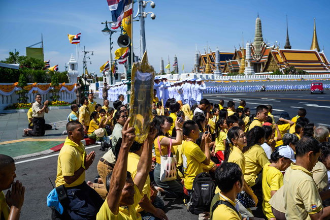 泰王和王后乘坐王家汽车，沿途有官员敬礼，穿上黄衣的民众在旁观看。（美联社）