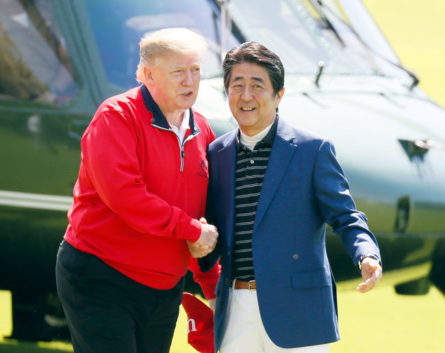 安倍在高尔夫球场的直升机坪迎接特朗普，两人握手带笑寒暄。