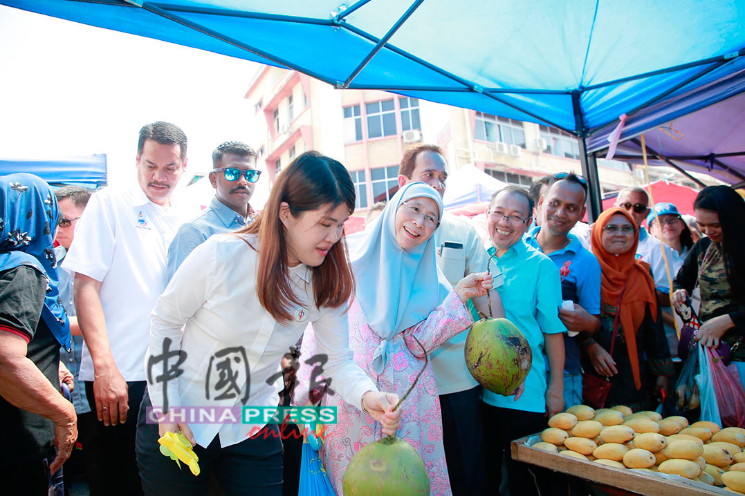 旺阿兹莎（前排右）路径市集水果档时，不忘拿起一颗椰子，表现出逗趣表情。