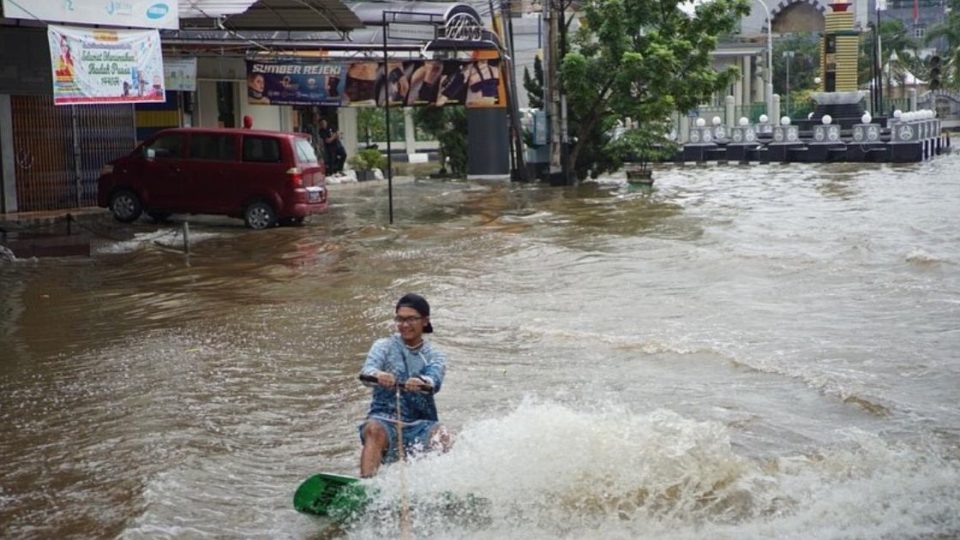 灾民在洪水中玩滑板冲浪。