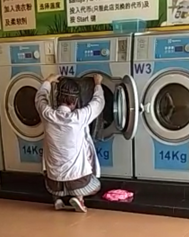 女子蹲在洗衣机前挑选所要的衣服。