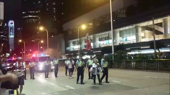 王婆婆手举英国国旗，后方由警察和警车护送。