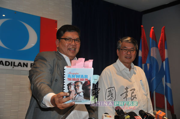 佐哈里（左）展示《为何安华不能当首相》书籍的手稿。旁为梁自坚。