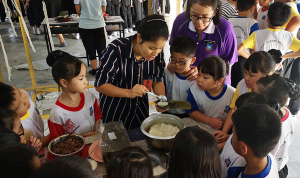 爱心妈妈教导学生包裹粽子的技巧，履行传承中华传统手艺的使命。