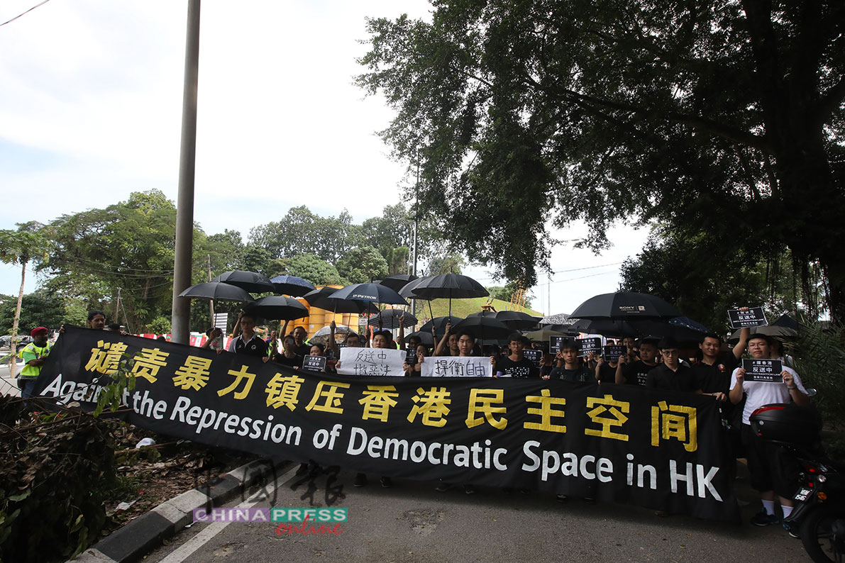 集会者手持横幅，谴责香港当局以暴力镇压当地民主。