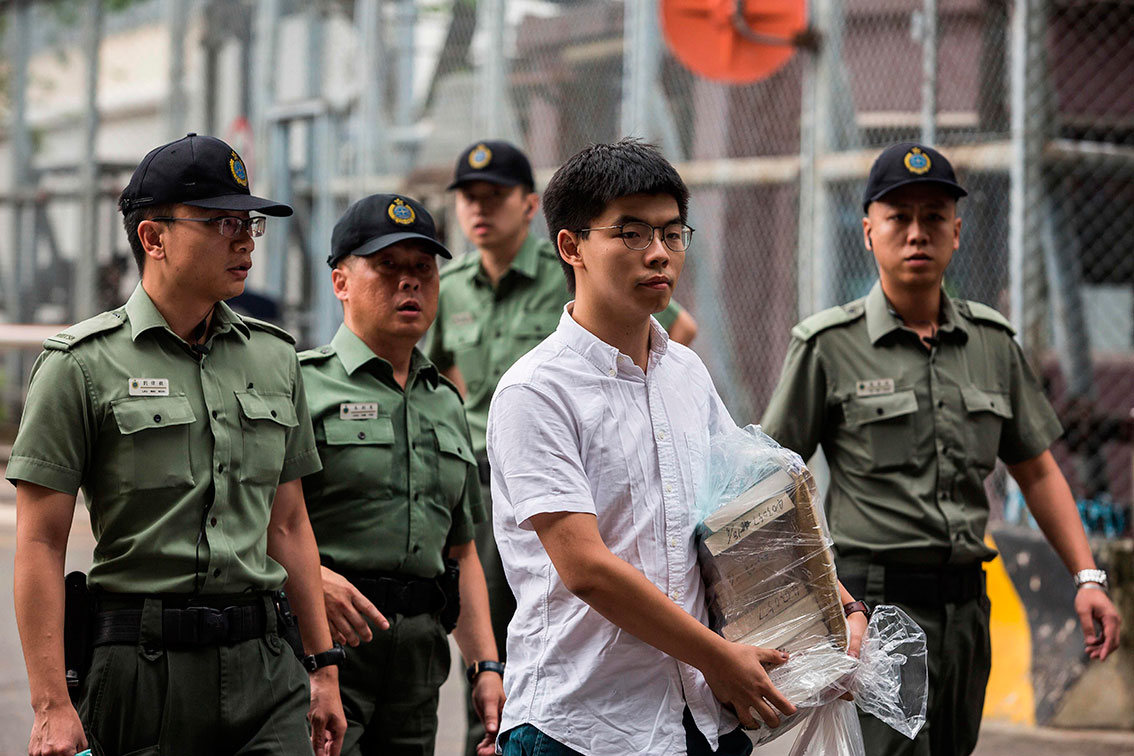 身穿白色衬衫的黄之锋，在警察护送下离开香港荔枝角收押所。 （法新社）