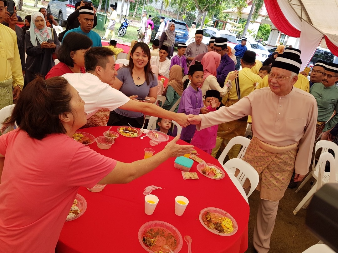 一身粉棕色马来传统服装打扮的纳吉（右）与到场共庆开斋节的华裔民众，握手问好。