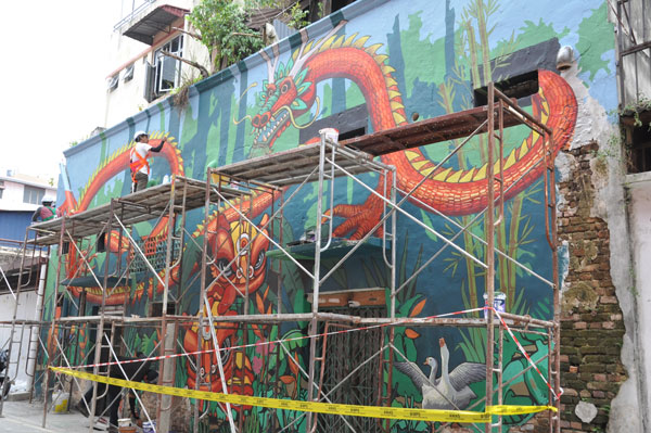 工人在荒废的商店后巷，画上充满中华文化色彩的龙及舞狮壁画。