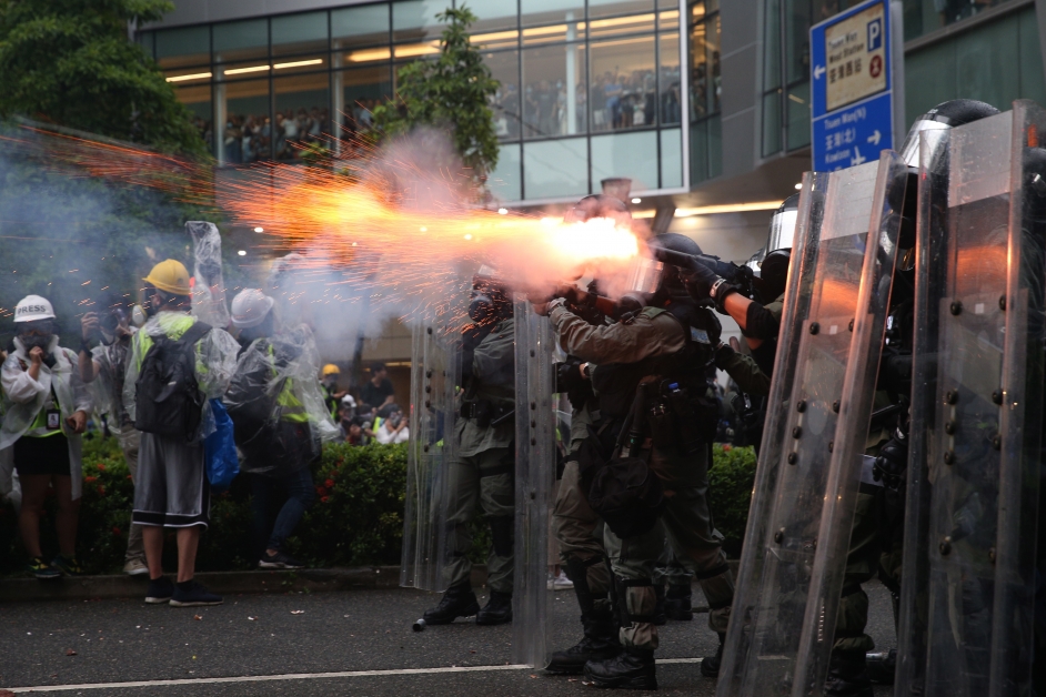 示威者正与警方对峙，警方举黑旗，其后发于催泪弹。