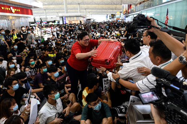 红衣女为了登机高举红色行李跨过数百示威者的照片引起讨论。（法新社）