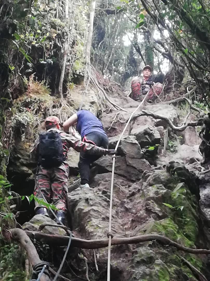 消拯员用绳子协助一名女生从山峰爬出。