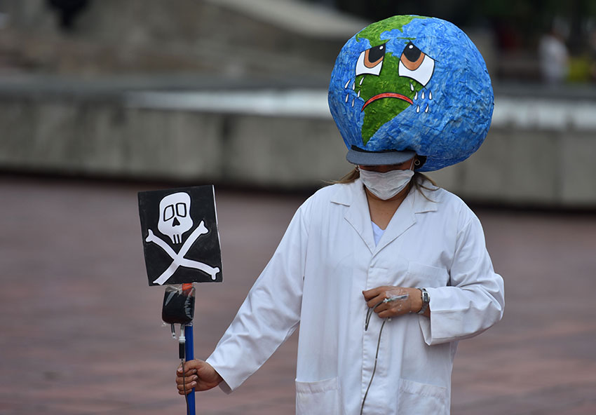 伦比亚一位参与气候示威的民众，头带着地球哭泣的头饰，一手持死亡标志，藉此传达不救地球人类必亡的讯息。（欧新社）