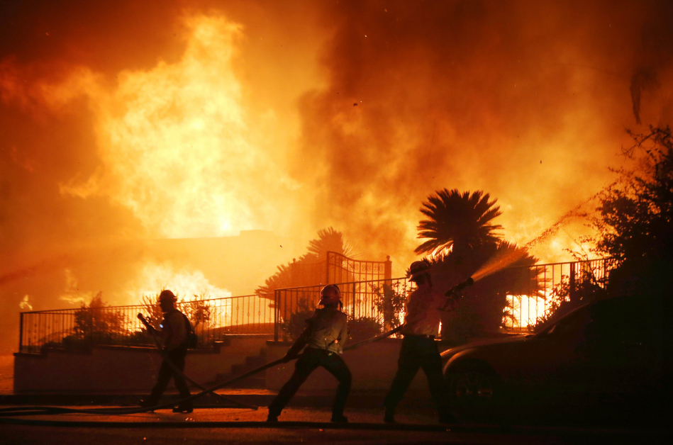 消防员周五在加州波特牧场一处起火房屋外奋力灭火。