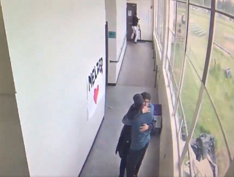 美国高中美式足球与田径教练洛威（下方蓝衣者）看到学生（下方黑衣者）拿着散弹枪进入学校，用爱的拥抱化解危机。（推特）