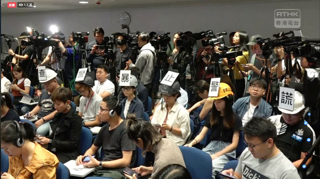 6名来自《立场新闻》、《明报》、《香港电台》、《端传媒》、《独立媒体》及《AM730》的记者，戴着贴有抗议文字的头盔出席记者会。