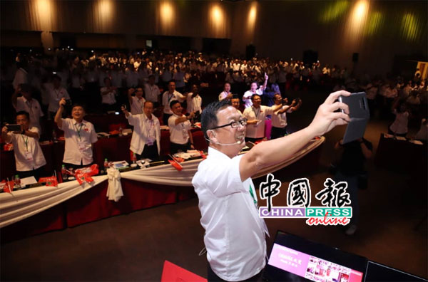 刘华才在台上用手机教在场党员如何自拍，而全体党员和元老也都配合拿出手机自拍。