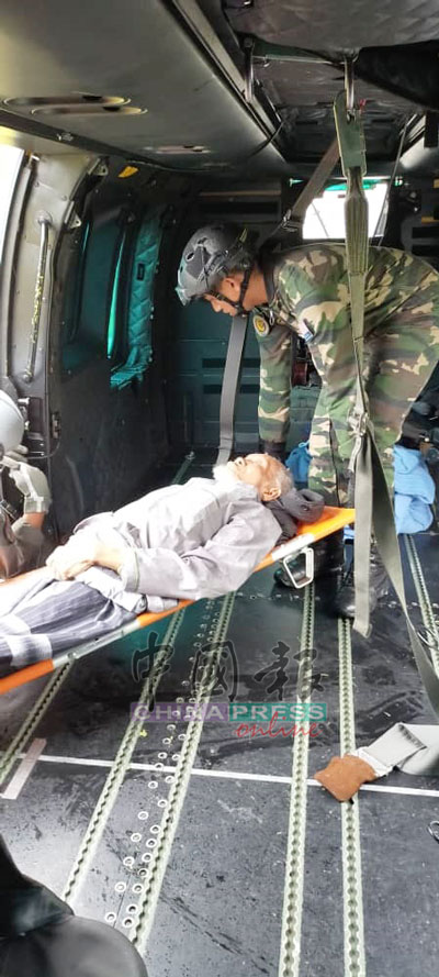 军人将一名行动不便的老人抬上直升机。