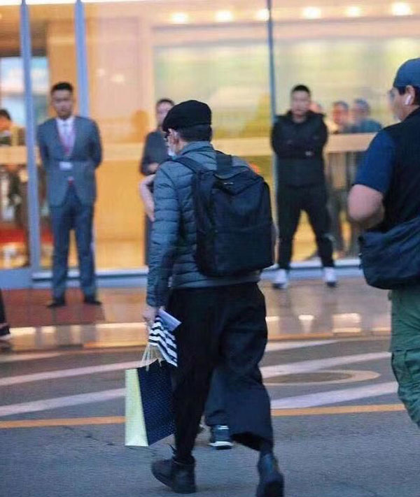 华仔背着背包，手拿着一袋礼物，一个人过马路离开。