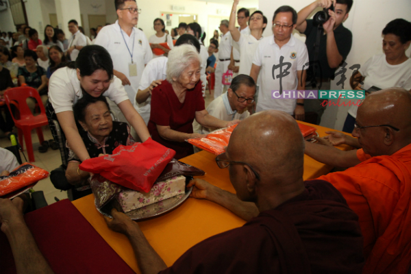 年长者在工作人员的协助下，为僧侣献上袈裟及化缘碗等物品。