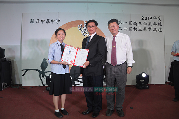 方天兴（中）在校长蔡若峰陪同下，移交毕业证书给一名高三学生。