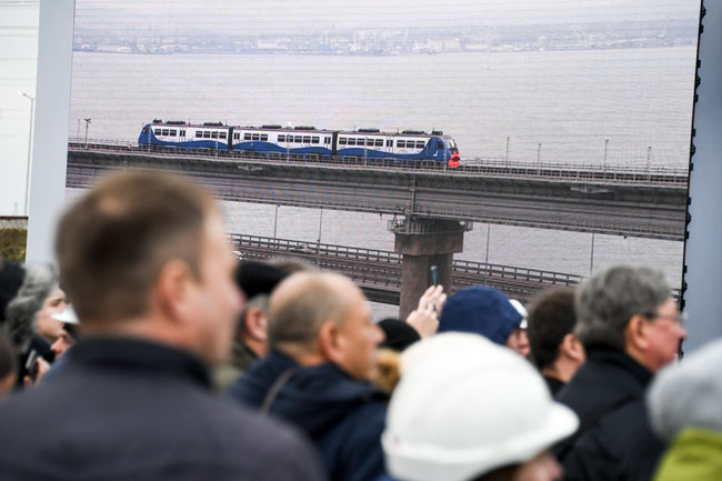民众周一透过大萤幕观看普汀搭乘火车通过克里米亚跨海大桥。（美联社）