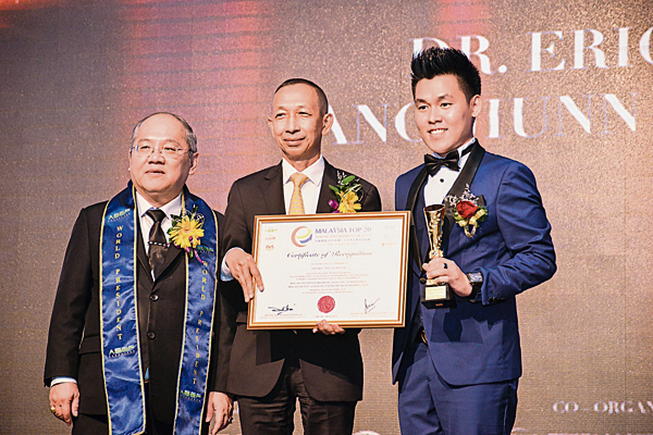 洪俊得（右）从颁奖嘉宾手中接过“马来西亚2019年度二十大杰出青年企业家”的奖状。